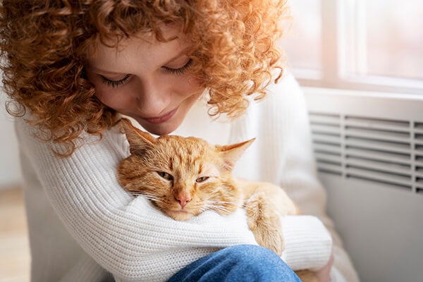 A woman smiling as she holds a relaxed cat in her arms